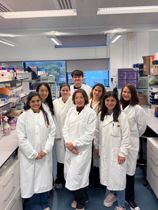 A group of eight people stood in the lab, wearing white lab coats, smiling at the camera.