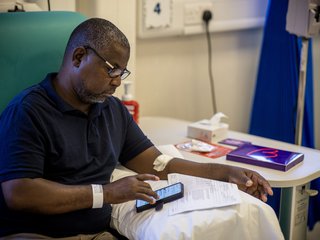 A man in hospital sits in a chair while reading his phone.
