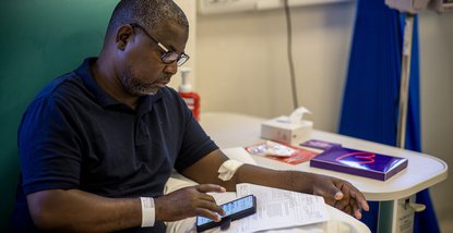 A man in hospital sits in a chair while reading his phone.