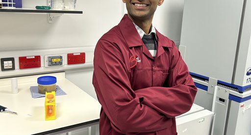 A man stood smiling in the lab with his arms folded wearing a red Blood Cancer UK lab coat.