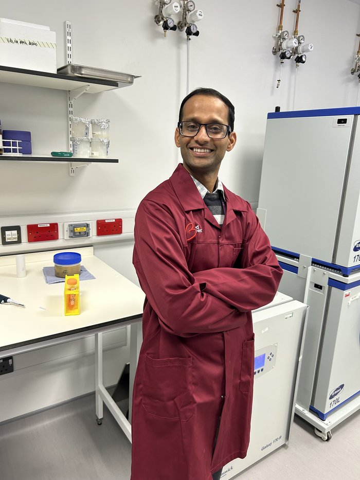 A man stood smiling in the lab with his arms folded wearing a red Blood Cancer UK lab coat.