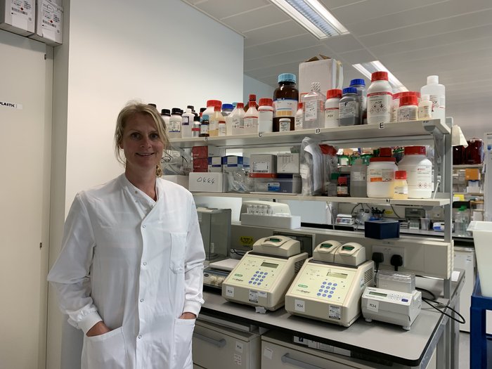 Dr Kristina Kirschner stood in the lab wearing a lab coat smiling at the camera.