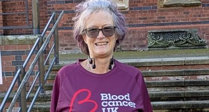 A smiling woman, wearing a Blood Cancer UK running top. She is standing in front of steps.