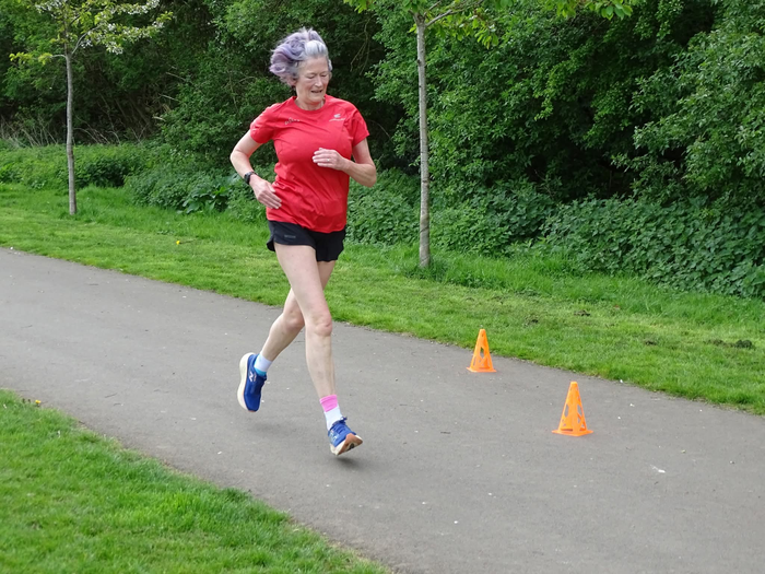 A woman running along a path in a park, next to some trees. She is wearing running gear.