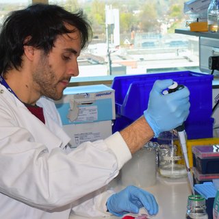 A man with dark hair wearing a white lab coat sat working in the lab.