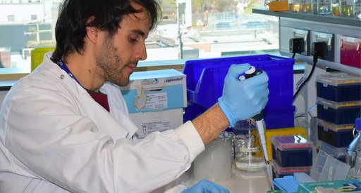 A man with dark hair wearing a white lab coat sat working in the lab.