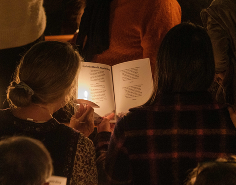 Over the shoulder view of a book with the carols lyrics taken in candlelight
