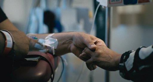 A patient and another person hold hands. The patient has an IV in their arm and a wristband on.