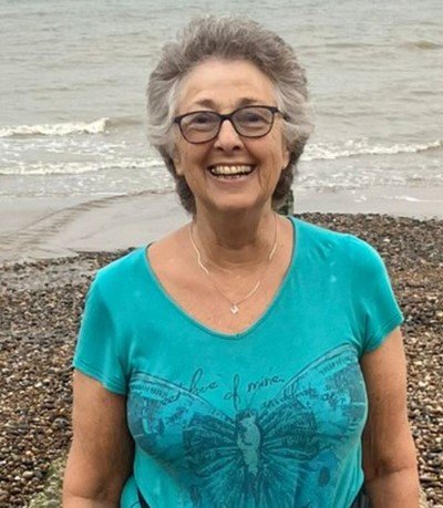 Marilyn on a pebbly beach, with her back to the sea, smiling at the camera.