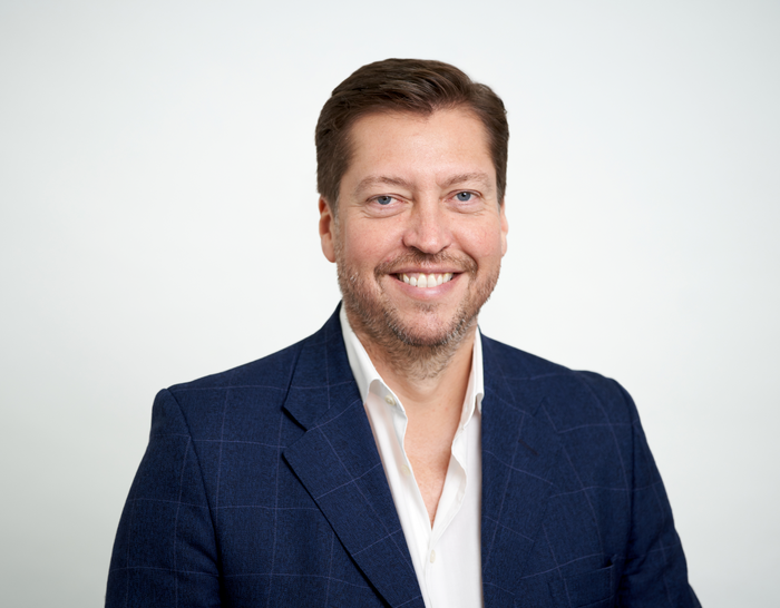 Matthew Wilson, a member of the Board, smiling against a plan white background.