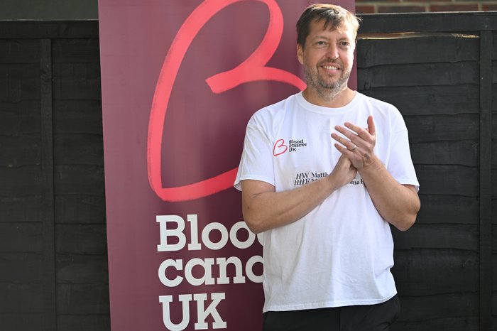Matthew clapping his hands stood by the Blood Cancer UK banner