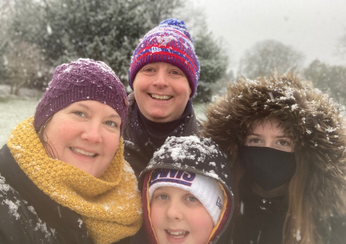 A family wearing coats, scarfs and winter hats, smiling in the snow.
