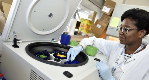 A researcher, wearing a white lab coat, in a lab loading a centrifuge.
