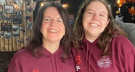 Nat and daughter wearing burgundy Walk of Light hoodie with their arms round each other