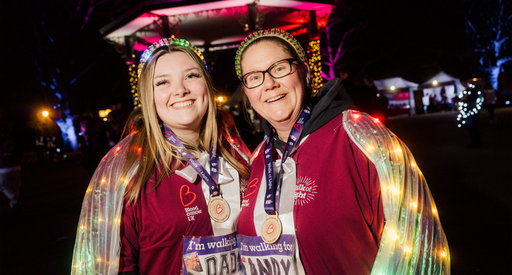 A mother and daughter stood together smiling wearing lights over their hair and wearing Walk of Light hoodies