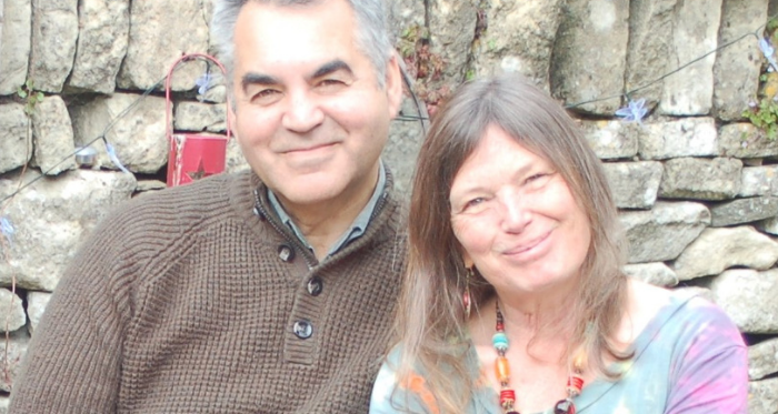 Nicky, a woman who lives with chronic lymphocytic leukaemia (CLL) and participated in a clinical trial, sits next to a man in front of a stone wall.