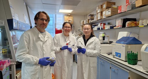 Dr Feldhahn in the stood in the lab with two members of his lab team, wearing white lab coats.
