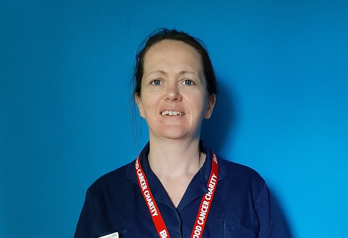 Alison, a blood cancer clinical nurse specialist, poses for a headshot in front of a blue background.