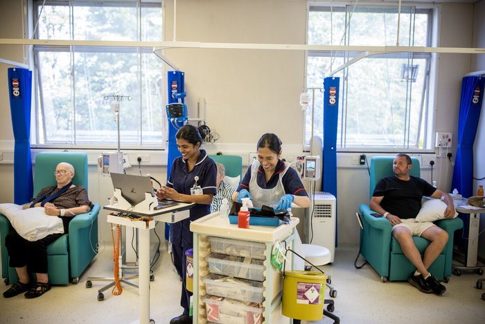 Nurses smiling on day unit with preparing medications. Two patients sit in chairs