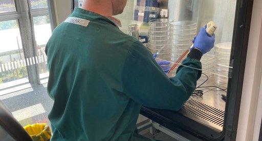 A man wearing a green lab coat sat working in the lab with his back facing the camera.