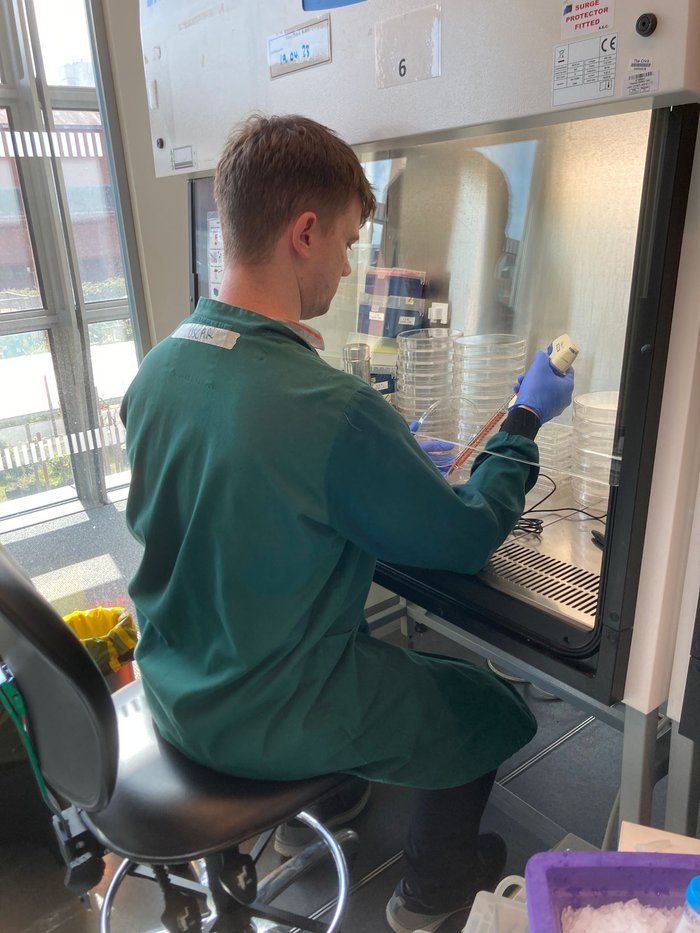 A man wearing a green lab coat sat working in the lab with his back facing the camera.