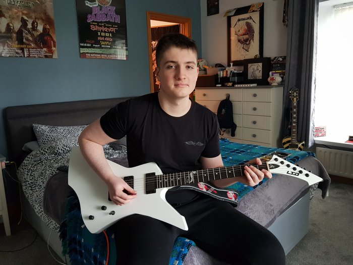 Ozzie, who lived with acute myeloid leukaemia (AML), sits in his bedroom holding a guitar.