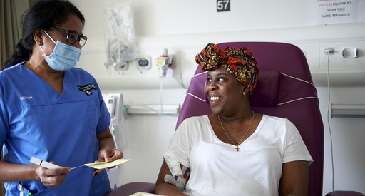 A nurse stands next to a patient sitting on a hospital bed in a treatment room.