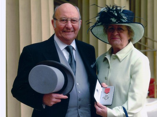 Ken Lomas, an Honorary President of Blood Cancer UK, and his wife holding a medal in front of marble columns.