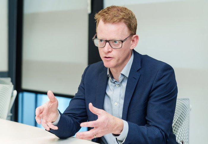 A man in a suit sat at a table explaining his research to others