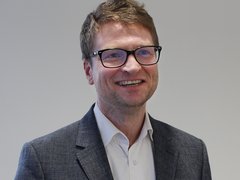 A headshot of a man in a suit wearing glasses smiling at the camera.