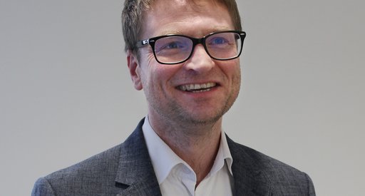 A headshot of a man in a suit wearing glasses smiling at the camera.