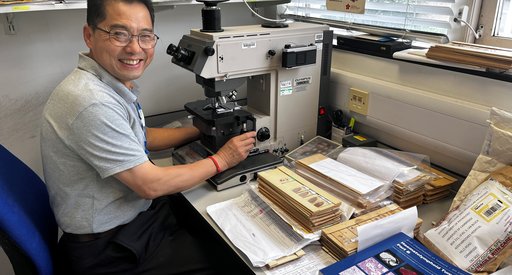 Professor Ming Du sat working at a microscope in the lab, facing the camera whilst smiling.