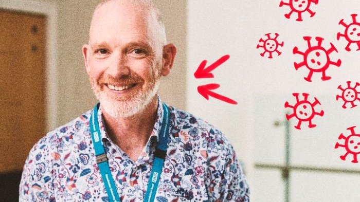 Image of a man with a grey beard and brown eyes, wearing a blue NHS lanyard and colourful shirt smiling at the camera. Hand-drawn red blood cells in the top right hand corner.