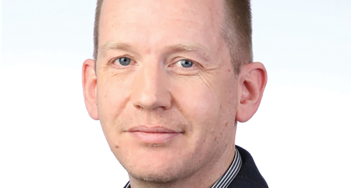 A headshot of a man with short, light brown hair and blue eyes. He is looking directly at the camera. His expression is neutral.