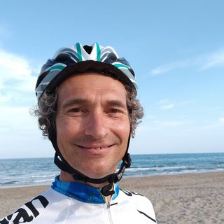 Quentin, who lives with acute myeloid leukaemia (AML), stands on a sandy beach wearing cycling clothes and a helmet.