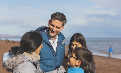 A group of people stand on a beach with the sea in the background.