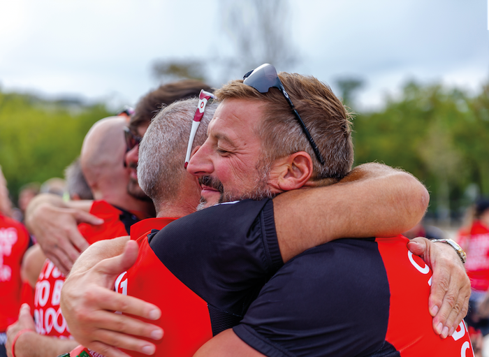 Close-up of Blood Cancer UK supporters wearing branded clothing hugging and smiling at a sports event.