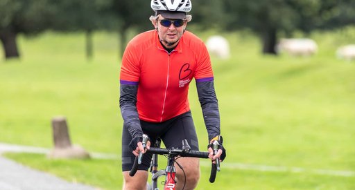 Cyclist in a park wearing sunglasses and a Blood Cancer UK cycling jersey.