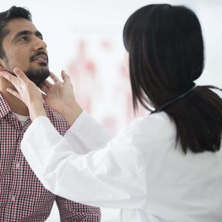 Doctor examining patient's throat by feeling for swollen lymph nodes in examination room.