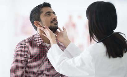 Doctor examining patient's throat by feeling for swollen lymph nodes in examination room.
