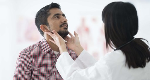 Doctor examining patient's throat by feeling for swollen lymph nodes in examination room.