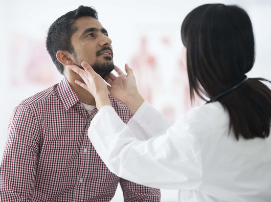 Doctor examining patient's throat by feeling for swollen lymph nodes in examination room.