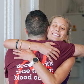 Two people hug and smile, wearing a Blood Cancer UK t-shirt.