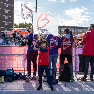 People standing with their backs to the camera at a cheering point, all wearing Blood Cancer UK t-shirts.