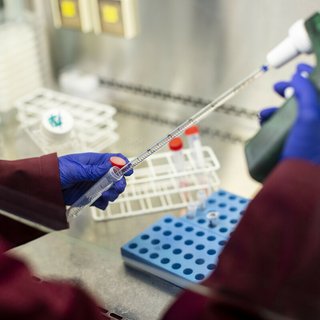A close up of a researcher's hands in a lab, holding a pipette and test tubes.