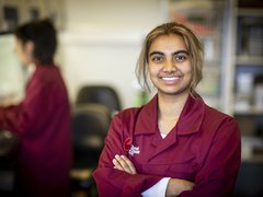 A researcher smiles at the camera, wearing a burgundy Blood Cancer UK lab coat