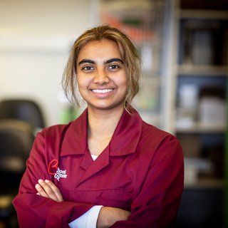 A researcher smiles at the camera, wearing a burgundy Blood Cancer UK jacket