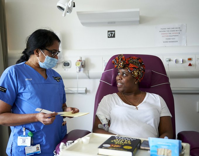 A healthcare professional and patient looking at each other. The patient is sitting in a chair having treatment administered.