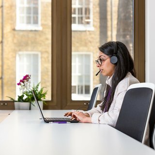 Woman talking on the phone with headphones and computer.