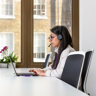Woman talking on the phone with headphones and computer.